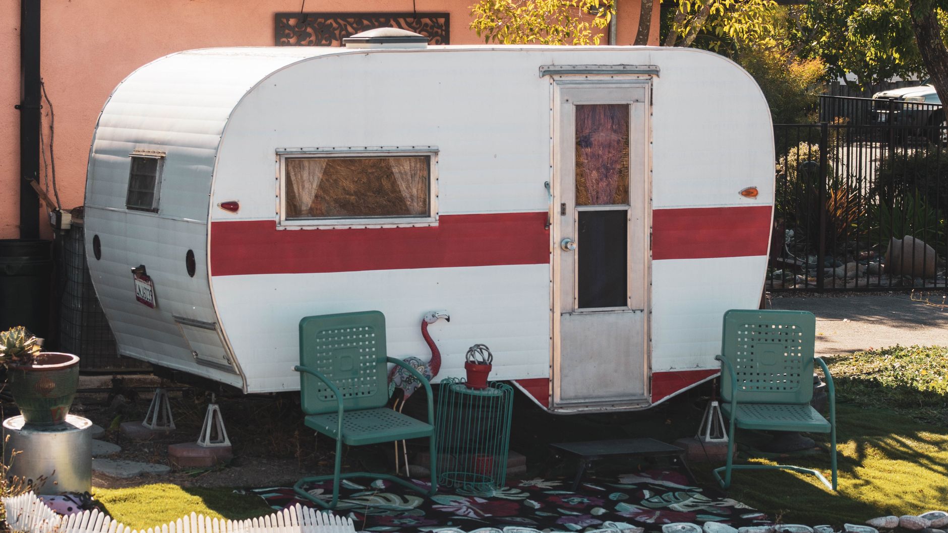 Restored red-striped vintage trailer with flamingo lawn ornament and vintage chairs